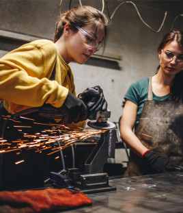 Two female apprentices learning how to cut metal in a workshop