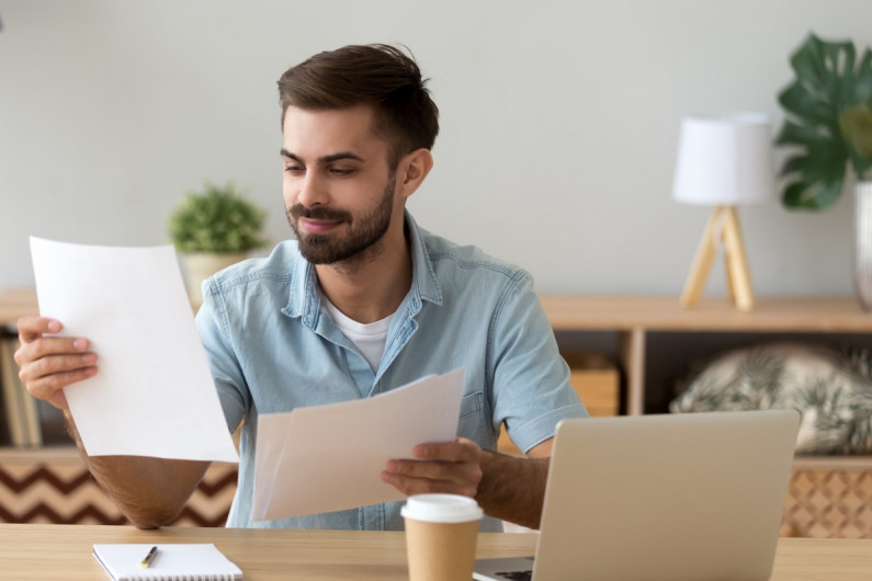 Smiling man sitting at a desk reading one sheet of paper