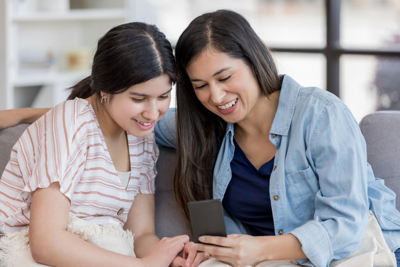 A woman and her high-school student daughter smile at a cellphone.