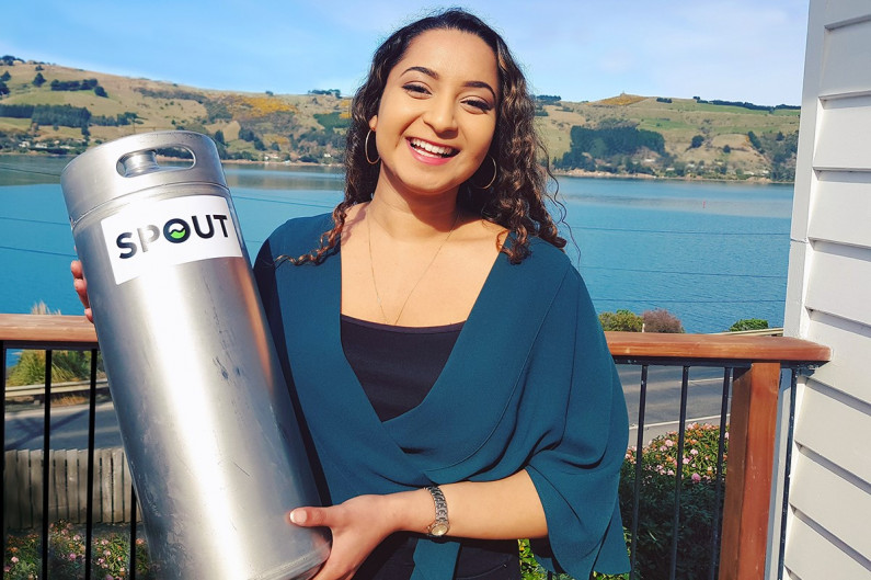 Jo Mohan holds a metal keg in front of a view of the sea