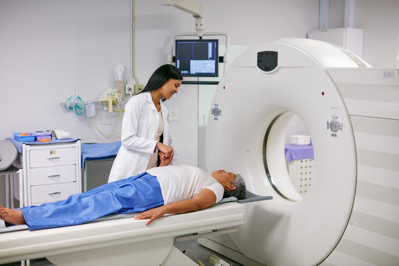 A medical imaging technologist holds a patient's hand as he's about to enter a scanner