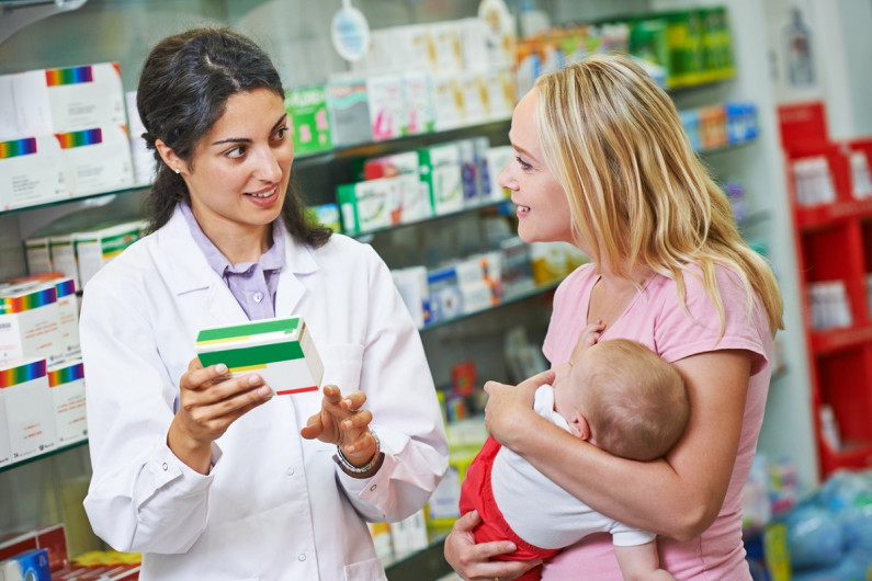Pharmacist talking to mother with baby in pharmacy