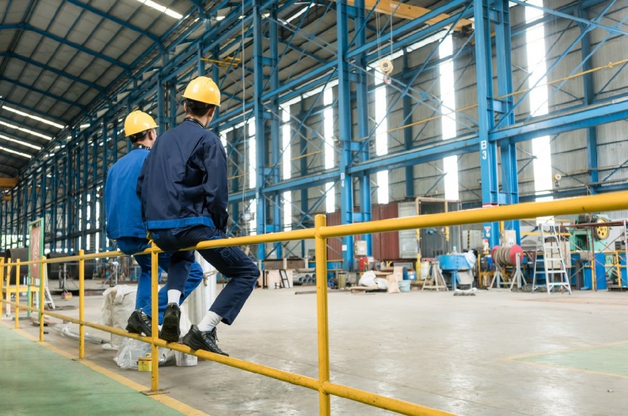 Two factory workers sit on a rail