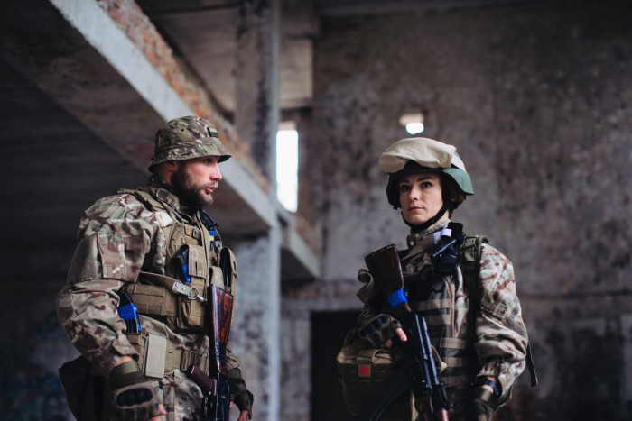 A man and woman soldier in full camoflage holding guns inside an empty building 