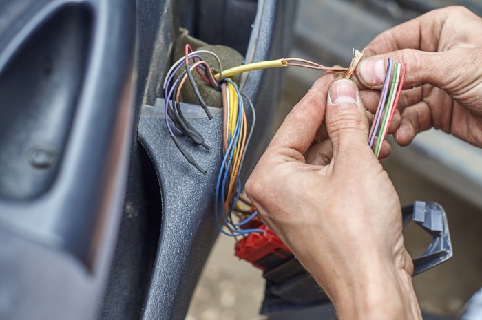 Close-up of hands working on some stripped wires coming out of a car door 