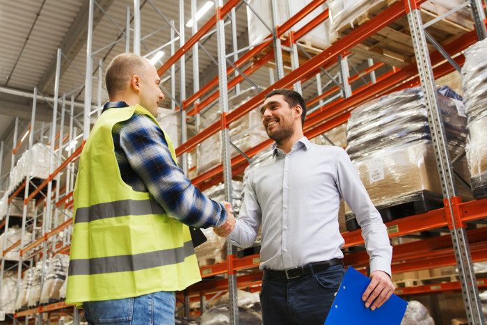 A buyer and supplier shaking hands in a warehouse after making a deal
