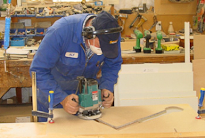 A cabinet maker uses a sanding machine on a piece of timber.