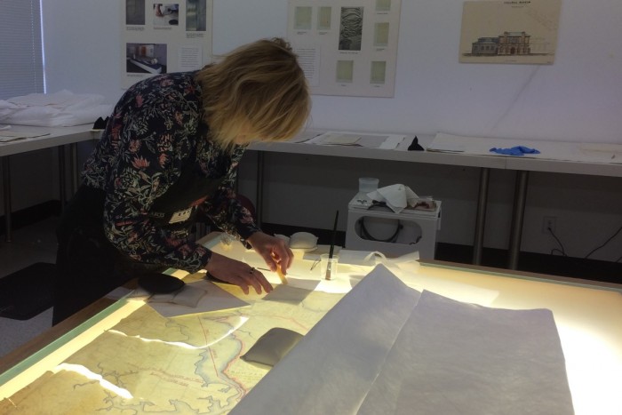 Anna Whitehead stands over a light table fixing a badly damaged map 
