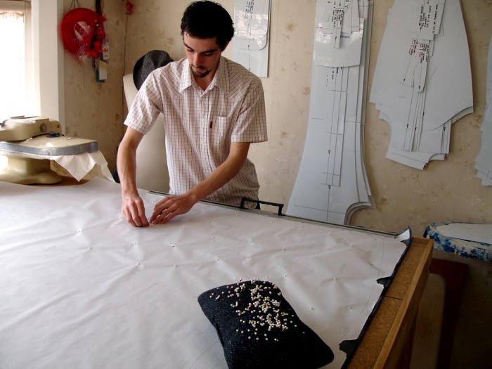 Ra Thomson standing at a workbench pinning pattern to fabric in studio