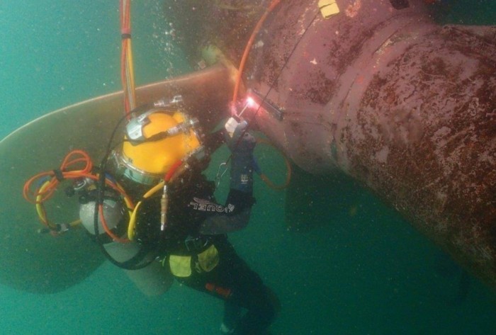 A diver underwater doing welding work on a ship's propeller