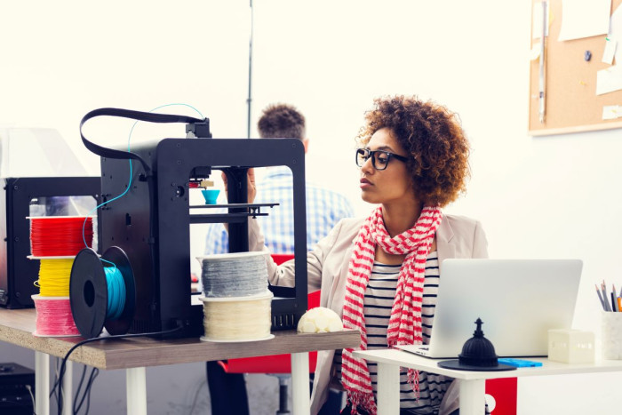 A woman watches a 3D printer produce a cup 