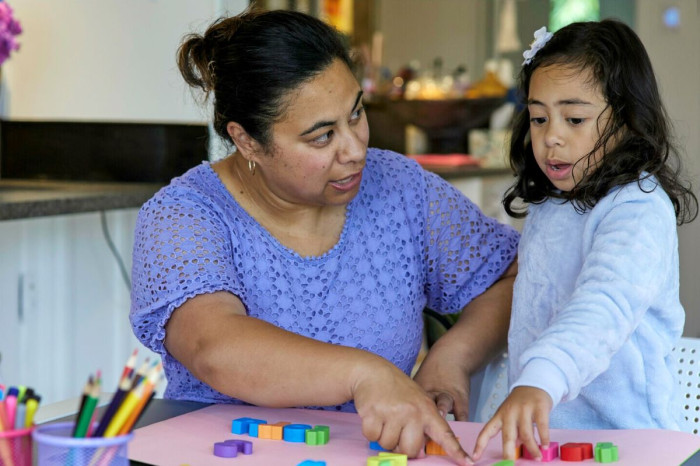 A female kaiwhakaako and a child pointing to a coloured block on a table in a classroom 