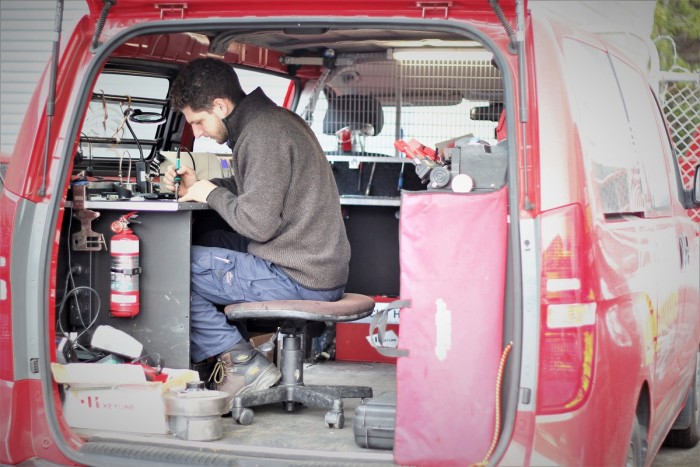 Dion Di Leva sits soldiering at a workbench in a mobile locksmith workshop van