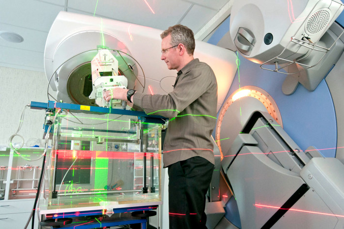 A male medical physicist standing and using a linear accelerator machine 