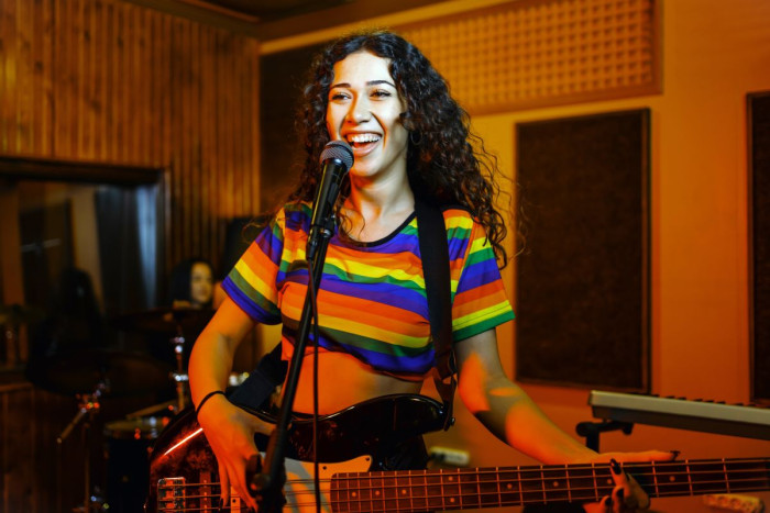 A female musician sings and plays bass guitar in a rehearsal room