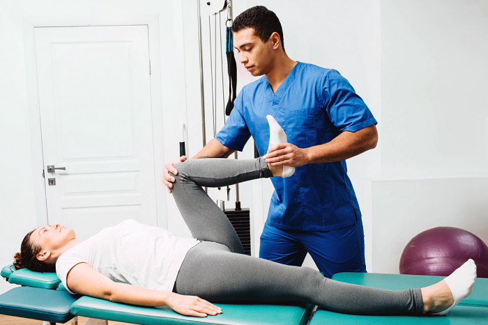A male osteopath treats a female patient by manipulating her leg muscles and joints
