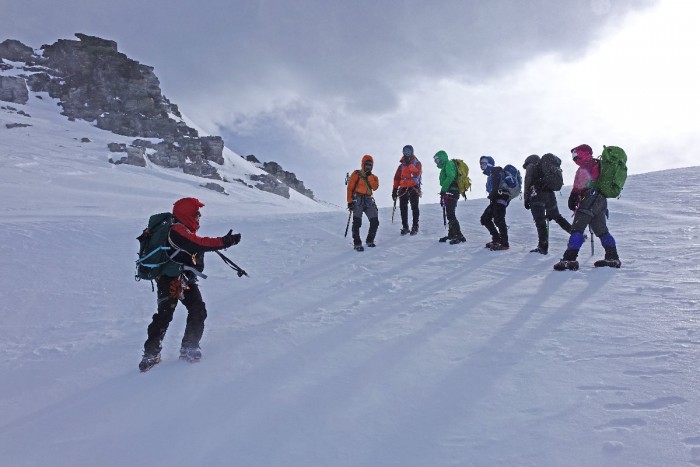 An outdoor recreation guide leading a group of people across a snow-covered slope