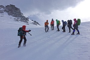 A group of skiiers on a mountain covered in snow are listening to a ski instructor.