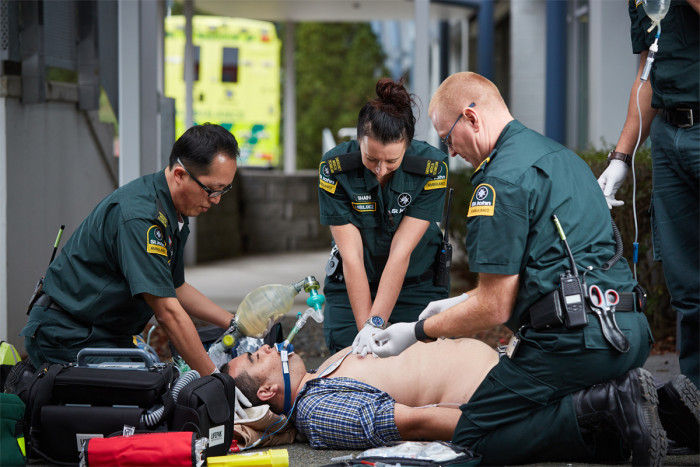 Three paramedics treat a patient lying on the ground with his shirt off
