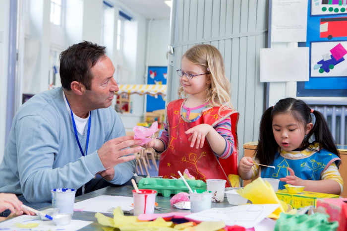 A man talks to two girls playing in a classroom