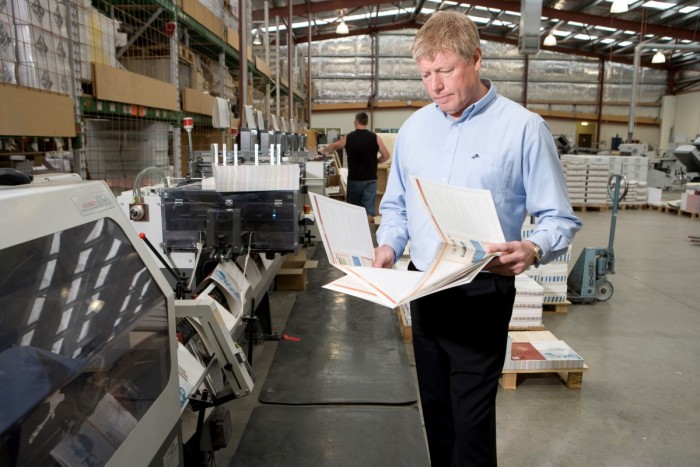 A print finisher standing by print finishing equipment looking at a final product 