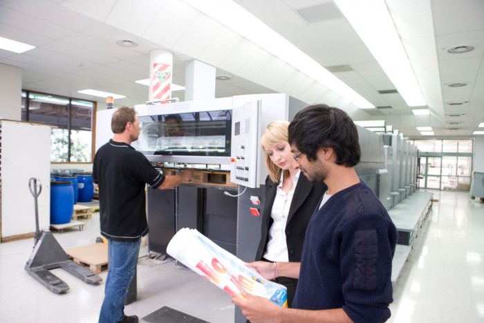A printer operating a print machine and clients looking at a poster 