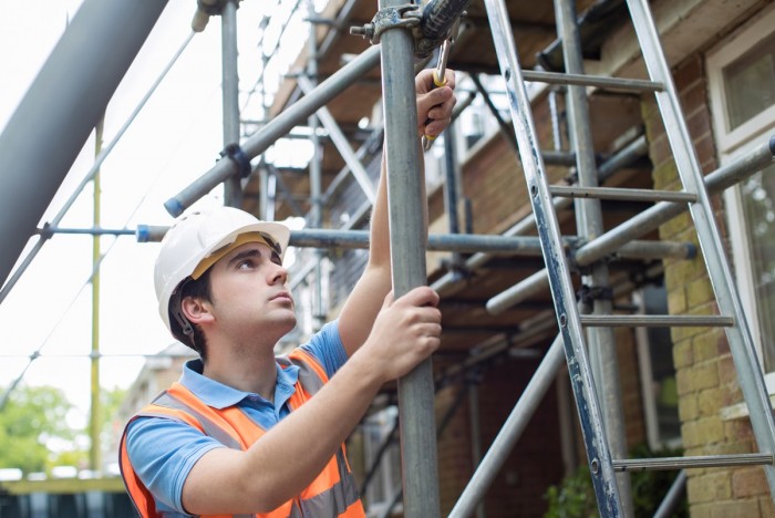 A man using a tool to tighten up a piece of scaffolding 