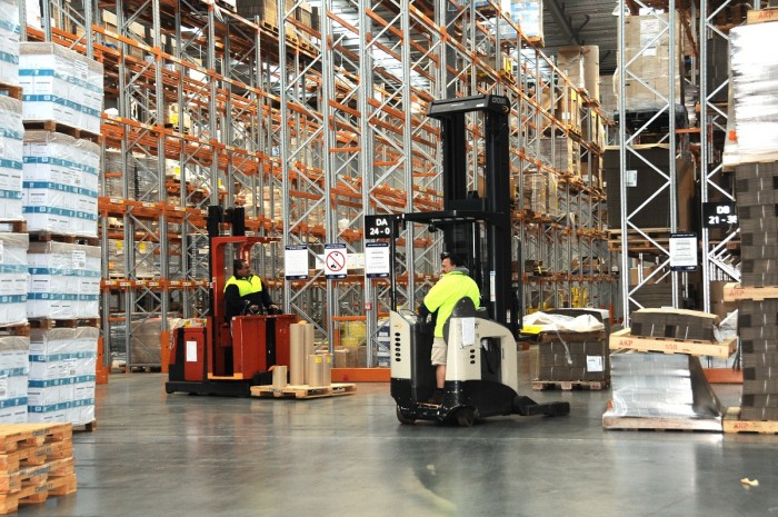Two storepeople operate forklifts in a warehouse
