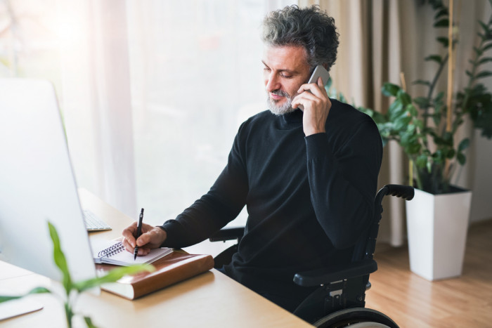 A male technical writer sitting in a wheelchair writing notes while talking on the phone