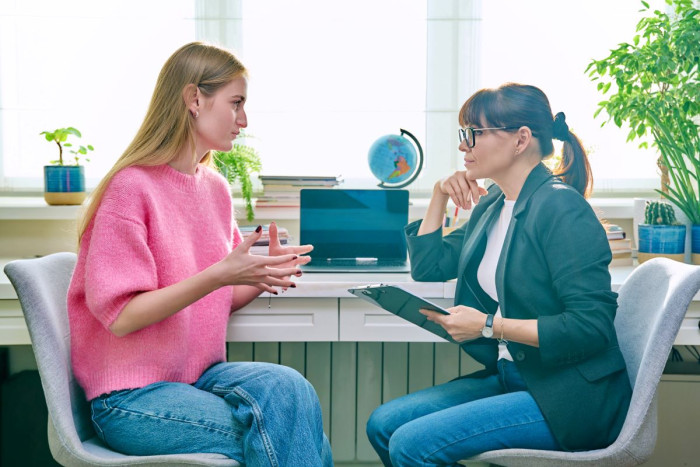 A teenage girl talks to an older woman who is taking notes, in an office